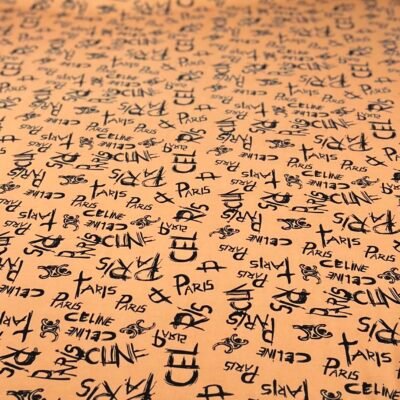 Close-up of peach-colored fabric covered with a repeating pattern of black fashion brand names such as Paris, Celine, and Chanel, with logos.