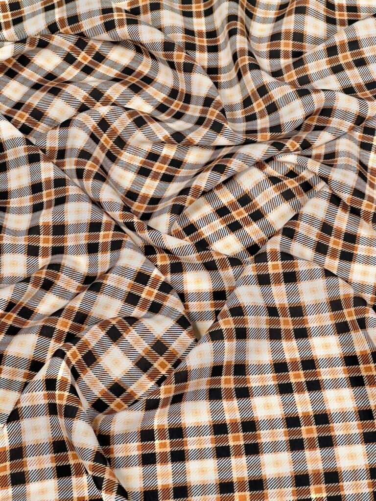 Close-up of plaid fabric in tan, black, and white with soft folds and texture.