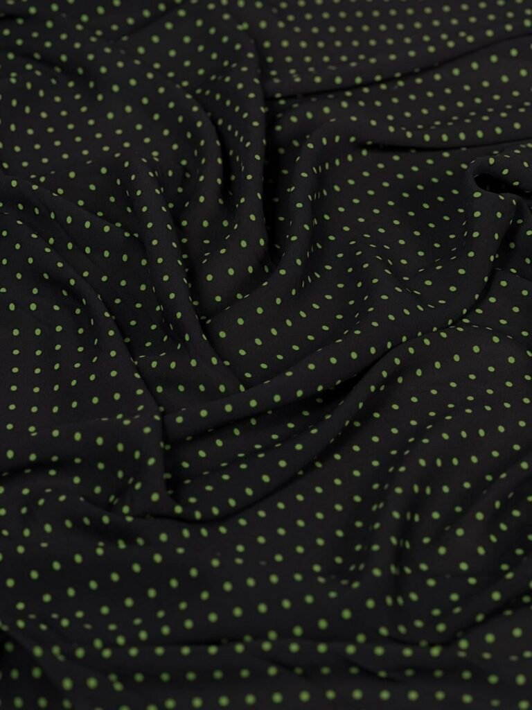 Black fabric with lime-green polka dots, softly draped and wrinkled.