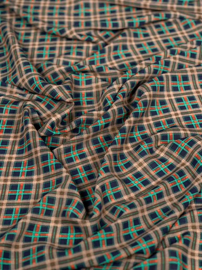 Close-up of plaid fabric in teal, red, and beige tones, with soft folds and creases throughout the material.