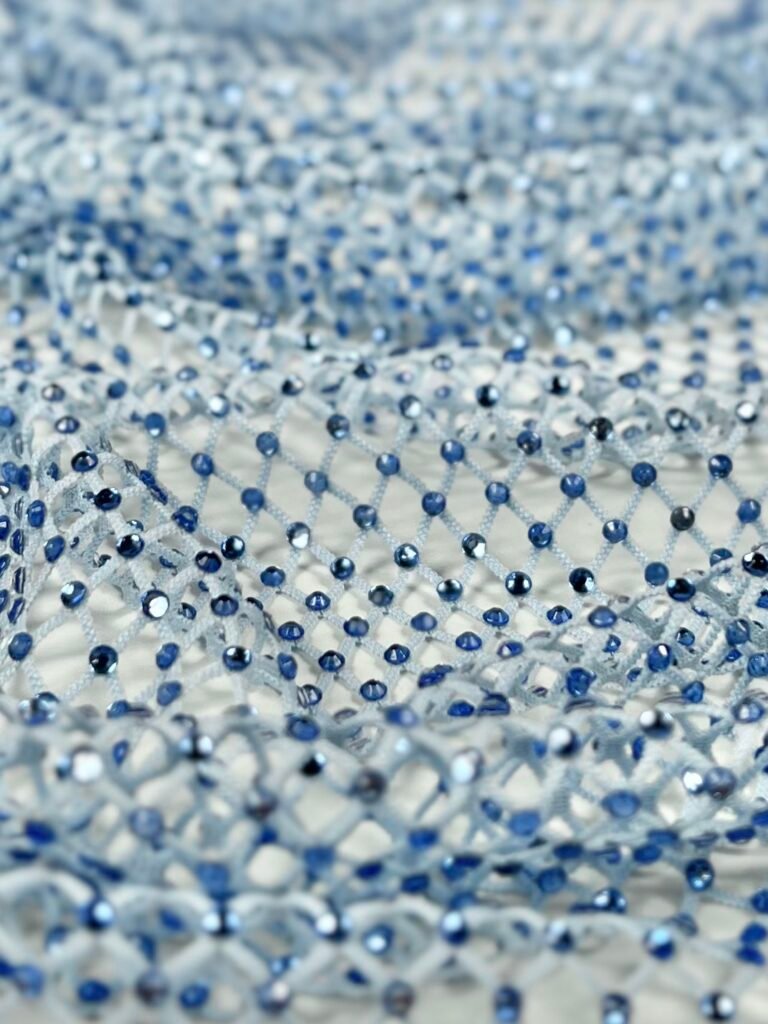 Close-up of a delicate net fabric adorned with small blue beads, creating a sparkling, textured pattern.