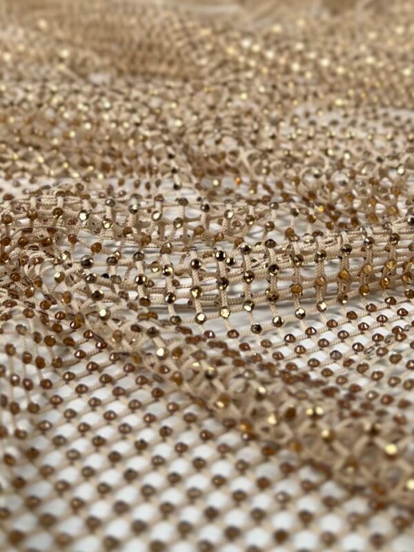 Close-up of gold sequin mesh fabric with tiny reflective beads in a grid pattern