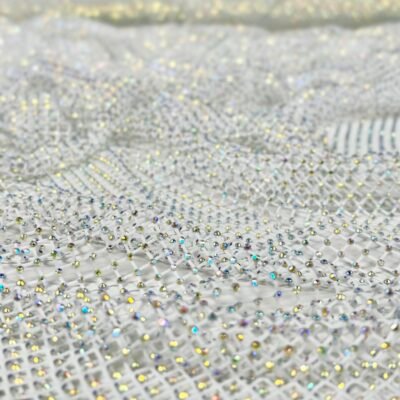 Close-up of sheer fabric covered in small iridescent rhinestones creating a sparkling pattern.