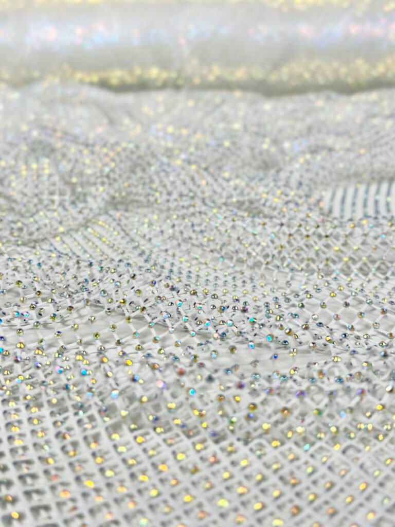 Close-up of sheer fabric covered in small iridescent rhinestones creating a sparkling pattern.