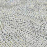 Close-up of white mesh fabric densely studded with tiny iridescent rhinestones, reflecting multicolored light.