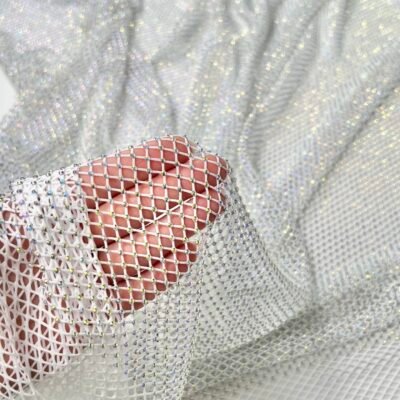 Hand holding shimmering silver mesh fabric with small rhinestones.