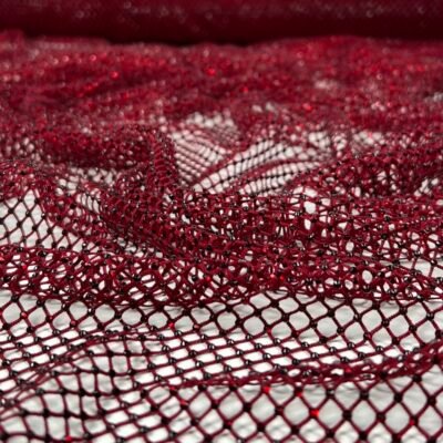 Close-up of deep red lace fabric with an open mesh pattern and tiny beads along the threads on a light background, showing intricate texture up close