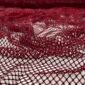 Close-up of deep red lace fabric with an open mesh pattern and tiny beads along the threads on a light background, showing intricate texture up close